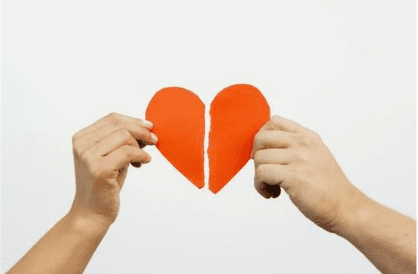 Two hands each hold one half of a red paper heart that has been torn down the middle, positioned against a plain white background.