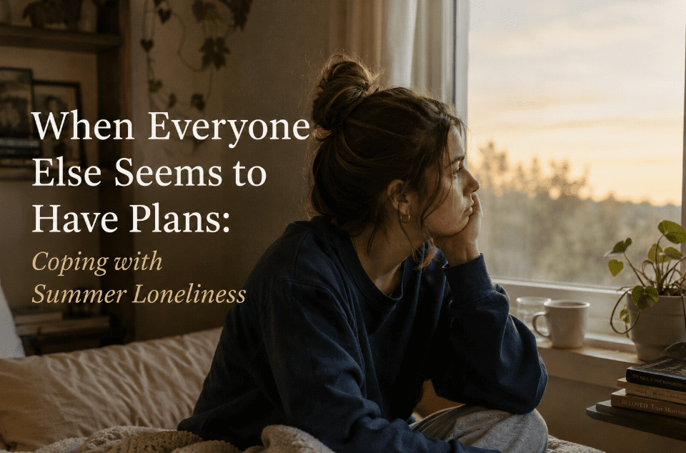 A woman sits on her bed by a window, looking thoughtfully outside. Text on the image reads: When Everyone Else Seems to Have Plans: Coping with Summer Loneliness. A mug and books rest on the windowsill.